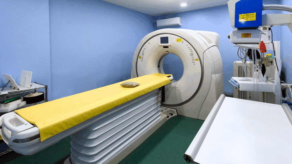 Una TAC con un tavolo imbottito di giallo è posizionata in una sala medica della Clinica Zarcone pulita e dalle pareti blu, circondata da varie attrezzature mediche e scaffali.